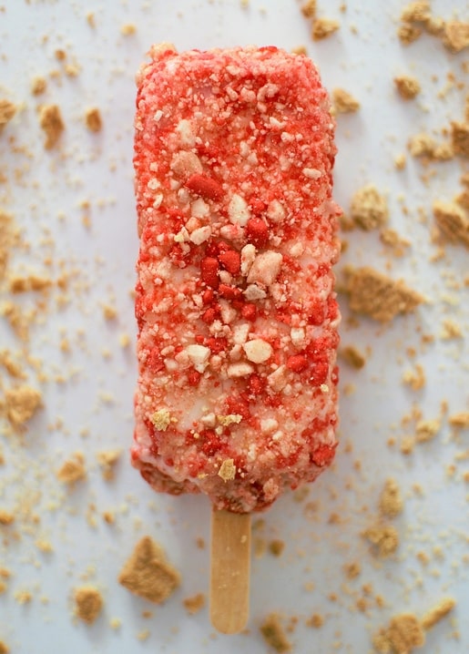 Eis am Stiel, gewälzt in rosa Erdbeerkrümeln und goldenem Keksstreusel