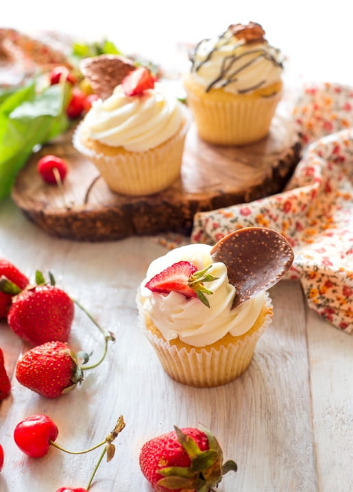 Vanille-Cupcake mit Sahne, Erdbeere und Schokoladenspan zwischen frischen Beeren