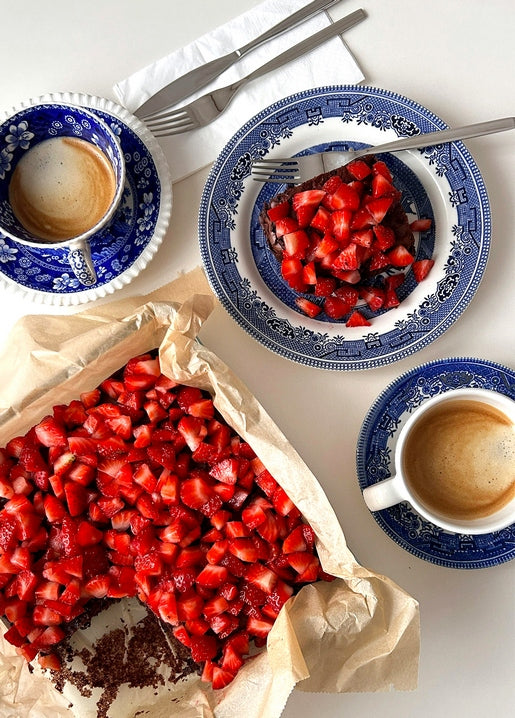 Strawberry tart on baking paper beside espresso cups in blue-and-white patterned china