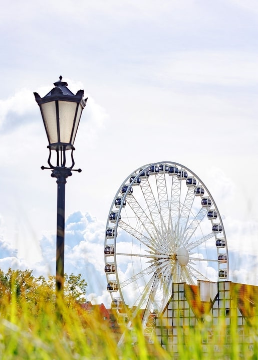 Ornate street lamp beside a towering Ferris wheel under a cloudy summer sky