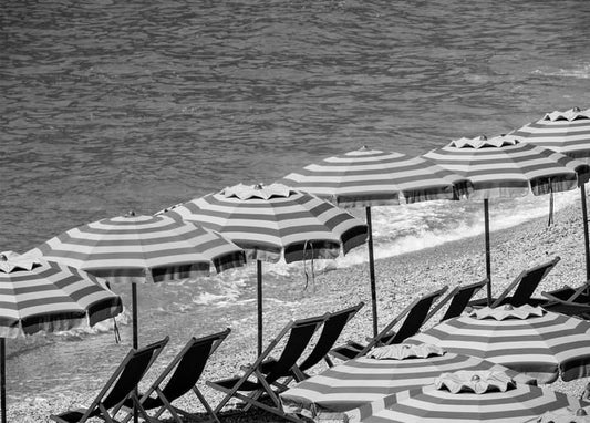 Black-and-white photo of striped beach umbrellas and lounge chairs on a pebble shore