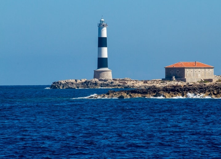 Schwarz-weiß gestreifter Leuchtturm auf einer Felslandzunge am Meer