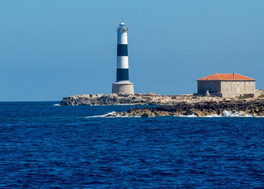 Black and white striped lighthouse on a rocky cape by the sea