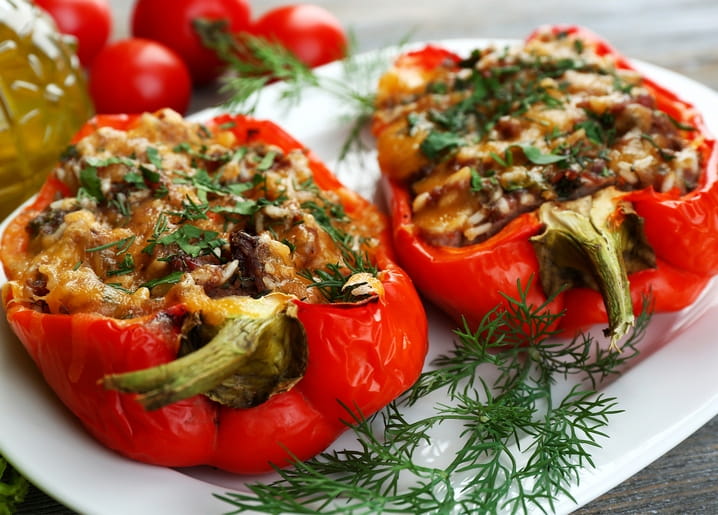 Zwei mit Reis gefüllte Paprika, überbacken mit Käse und Dill