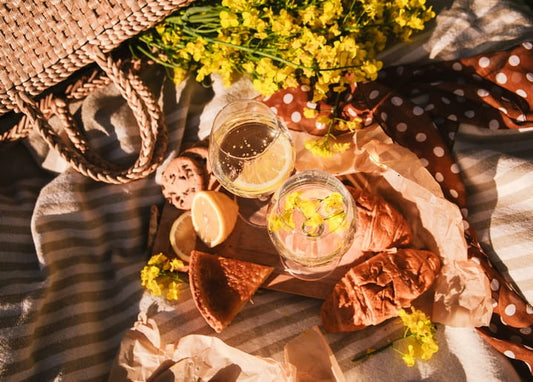 Picknick mit Weingläsern, Zitrone, Croissants und gelben Wildblumen auf einer gestreiften Decke