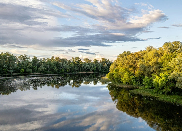 Calm river in Sumy region reflecting clouds and green forested banks at dusk
