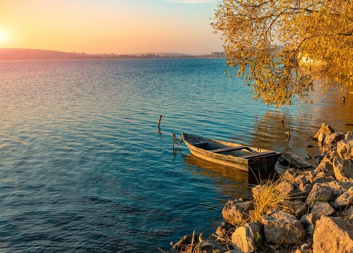Altes Holzboot am Ufer bei Sonnenuntergang mit herbstlichem Laub