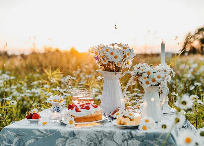 Sunset picnic table with daisies in white jugs, strawberry cake, and a glass of prosecco in a summer field
