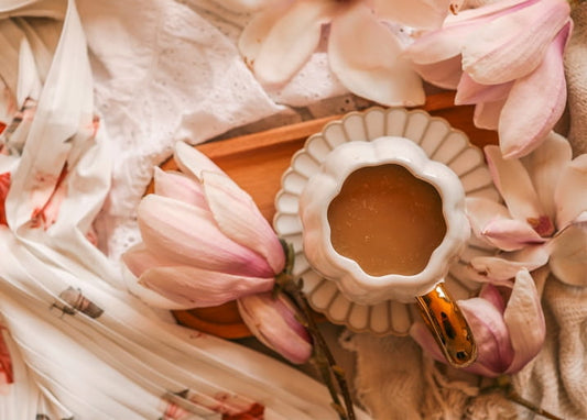 Scalloped white teacup with amber tea among scattered magnolia petals and lace