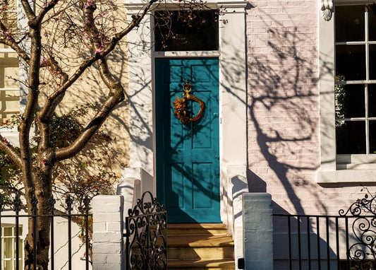 Teal front door with a dried-flower wreath beneath a blossoming tree