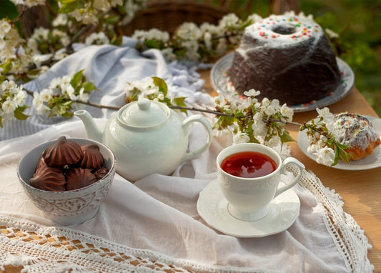 Weiße Teekanne, Tasse Tee und Kranzkuchen mit Pralinen unter Kirschblüten