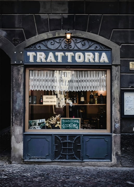 Dunkelblaue Trattoria-Fassade mit Lampe, Spitzenvorhängen und Küchenschild