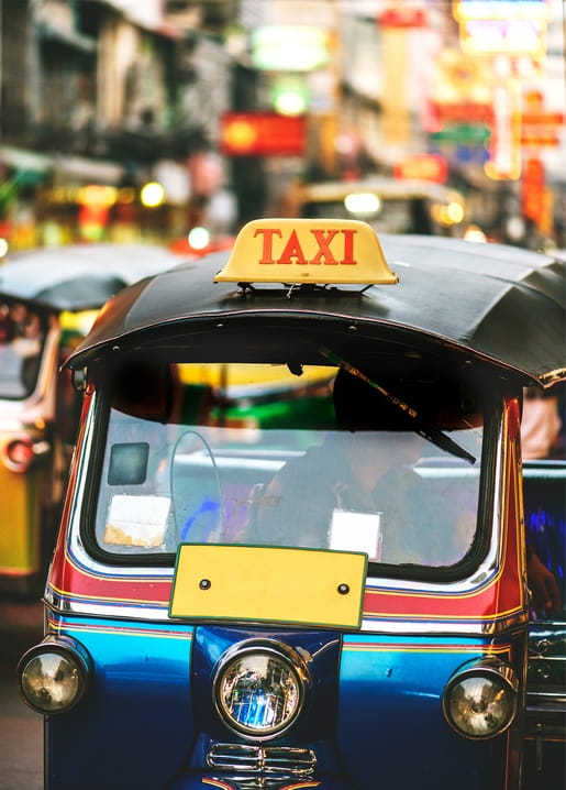 Vintage tuk-tuk taxi with a yellow TAXI sign parked on a street lit by blurred neon signs at night