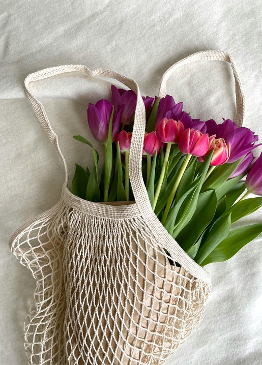 Purple and pink tulips spilling out of a cotton mesh shopping bag