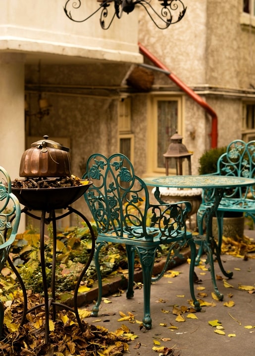 Türkise schmiedeeiserne Gartenstühle und ein Kupferkessel zwischen Herbstlaub