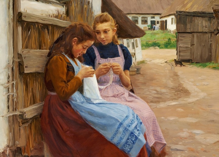 Two girls in Danish dress sewing against a barn wall with a black cat nearby