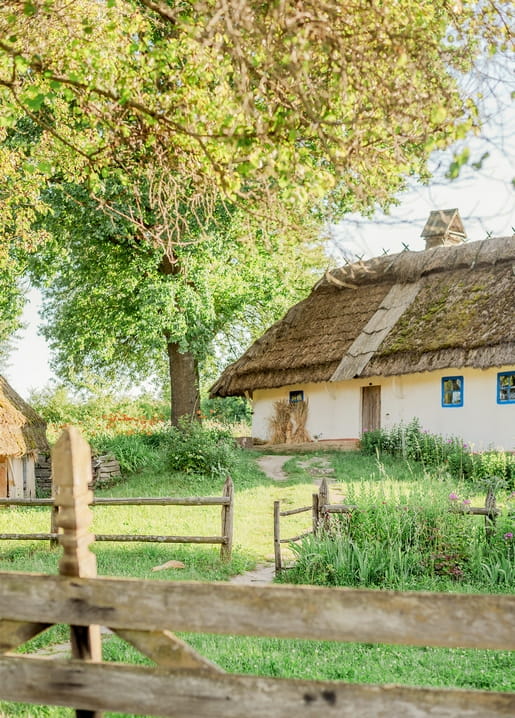Weißes ukrainisches Reetdachhaus mit blauen Fensterläden hinter einem Holzzaun