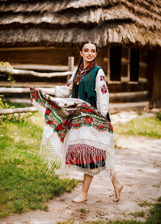 Дівчина у вишиванці з квітчастою хусткою біля хати під солом'яною стріхою
