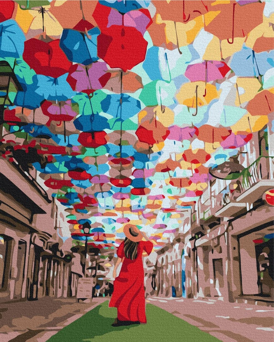 Bunte Regenschirme über einer Gasse, eine Frau im roten Kleid blickt hinauf