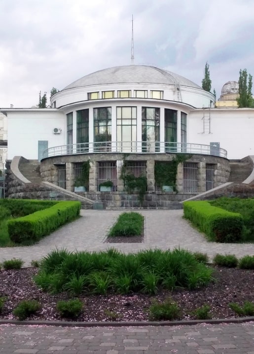 White rotunda entrance of Universytet metro station seen across a formal garden in Kyiv