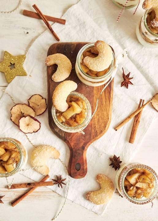 Vanilla crescent cookies and cinnamon apple compote jars on a wooden board with cinnamon and star anise