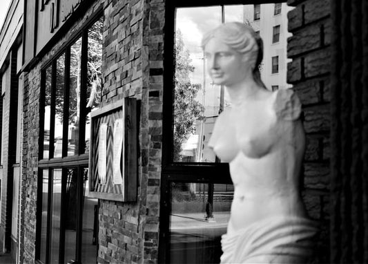 Classical Venus statue displayed in a brick building's shop window reflecting the street