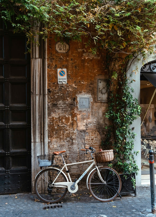 Cream vintage bicycle with wicker baskets against an ivy-covered brick wall