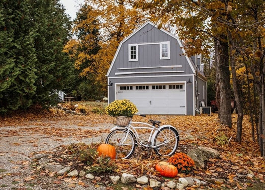 Weißes Vintage-Fahrrad mit gelben Chrysanthemen und Kürbissen vor einer grauen Garage