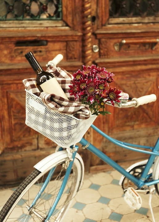 Blue vintage bicycle with a wine bottle and magenta chrysanthemums in its basket by a wooden door