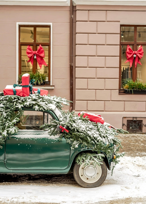 Vintage green car covered in fir branches and red gifts outside a pink building