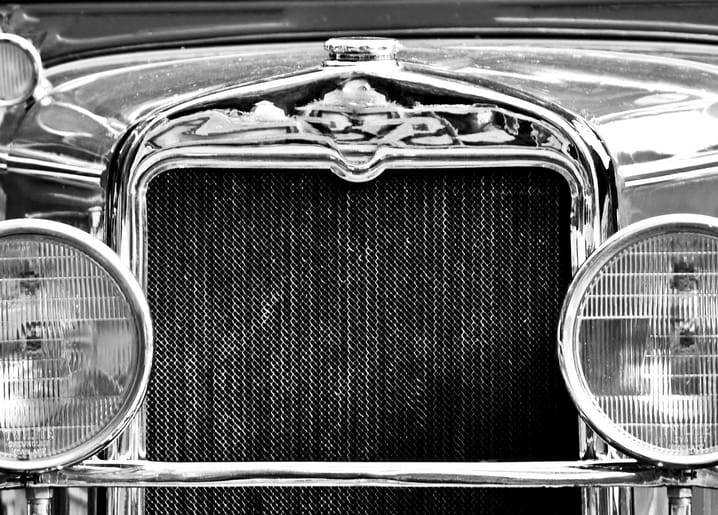 Nahaufnahme des verchromten Kühlergrills und runder Scheinwerfer eines Oldtimers, Schwarz-Weiß