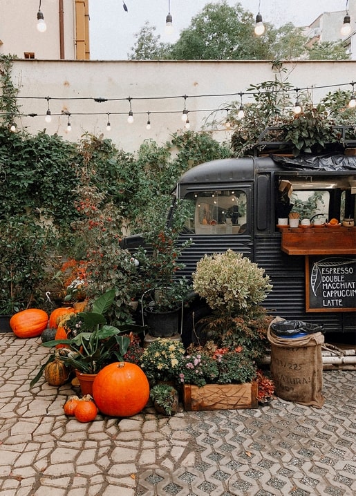 Dunkler Vintage-Kaffeewagen zwischen Kürbissen und Lichterkette im Hof