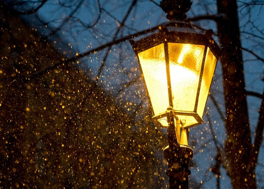 Vintage street lamp glowing at dusk with snow falling around it