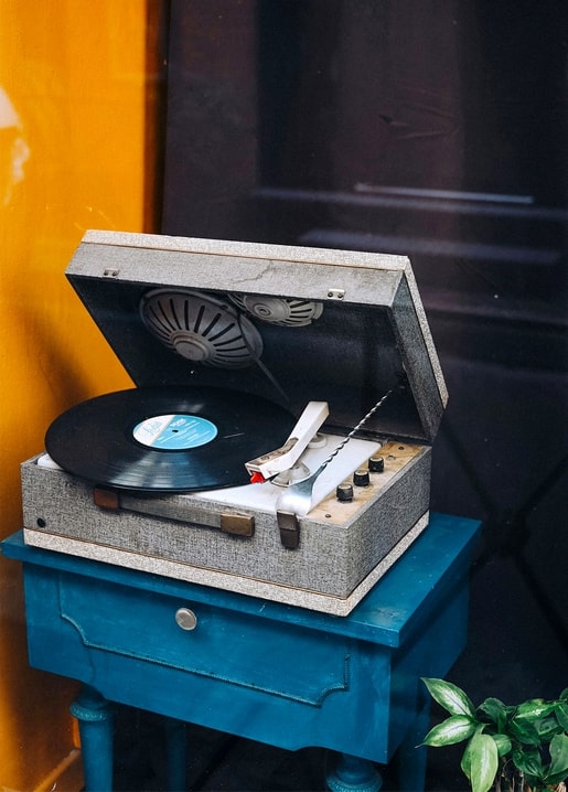 Vintage-Koffer-Plattenspieler mit laufender Schallplatte auf einem blau bemalten Tisch