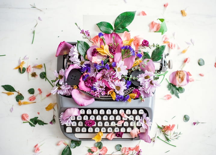 Vintage-Schreibmaschine, übersät mit rosa, violetten und gelben Blüten auf einer Marmorplatte