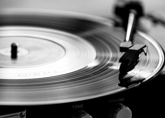 Close-up black-and-white photo of a vinyl record spinning on a turntable with tonearm