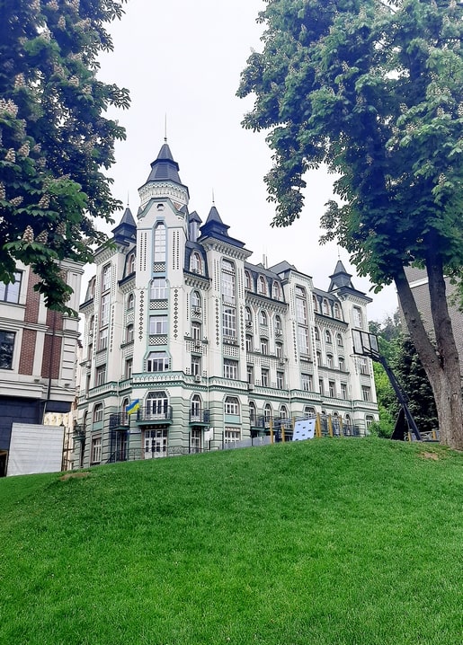 Turreted green-and-white tenement on Vozdvizhenka seen from a grassy Podil hill, Kyiv