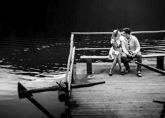 Couple in embroidered vyshyvanka sitting on a wooden pier by a lake, black-and-white photo