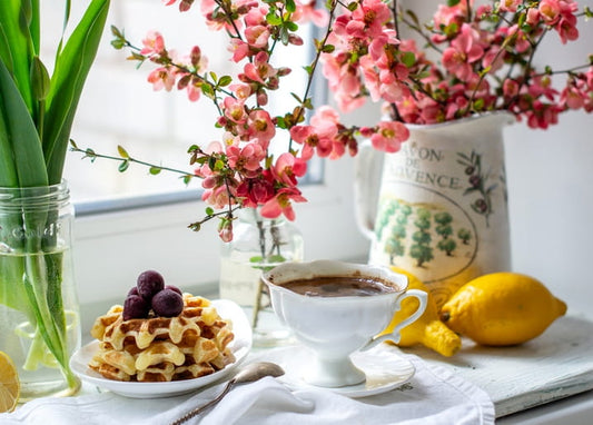 Waffles with berries, coffee and pink blossom branches on a sunlit table