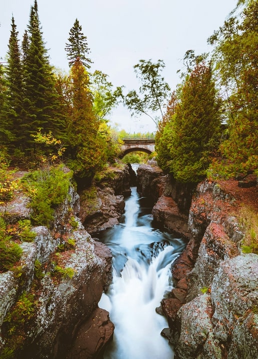 Wasserfall in einer herbstlichen Waldschlucht mit alter Steinbrücke
