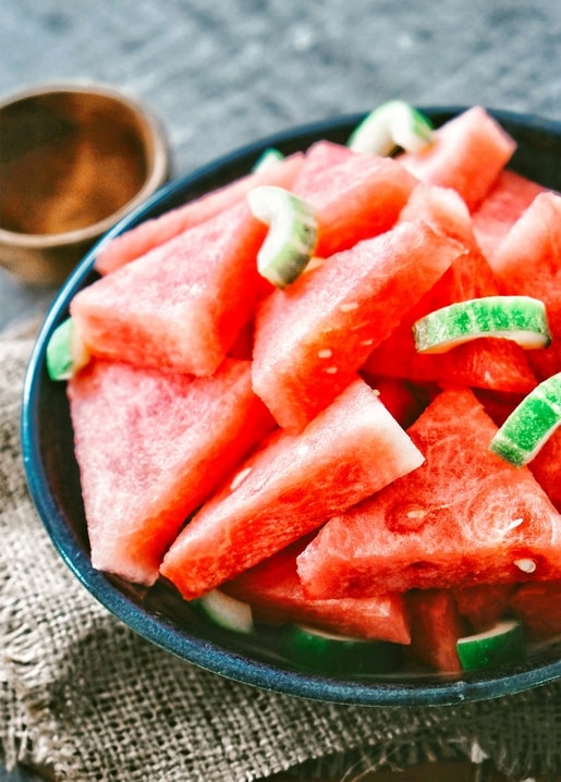 Wassermelonenstücke mit Minzröllchen in dunkler Schale auf Jute