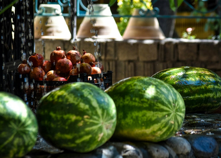 Watermelons and a crate of pomegranates on a sunlit stone market wall