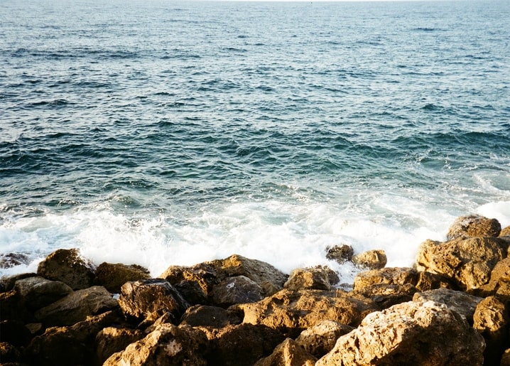 Turquoise waves break in white foam against golden rocks on a sunlit shoreline