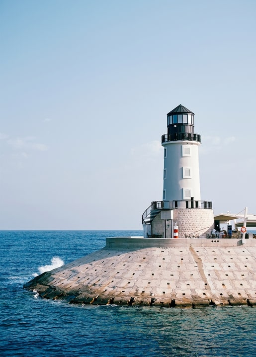 White lighthouse standing at the end of a stone breakwater by the sea