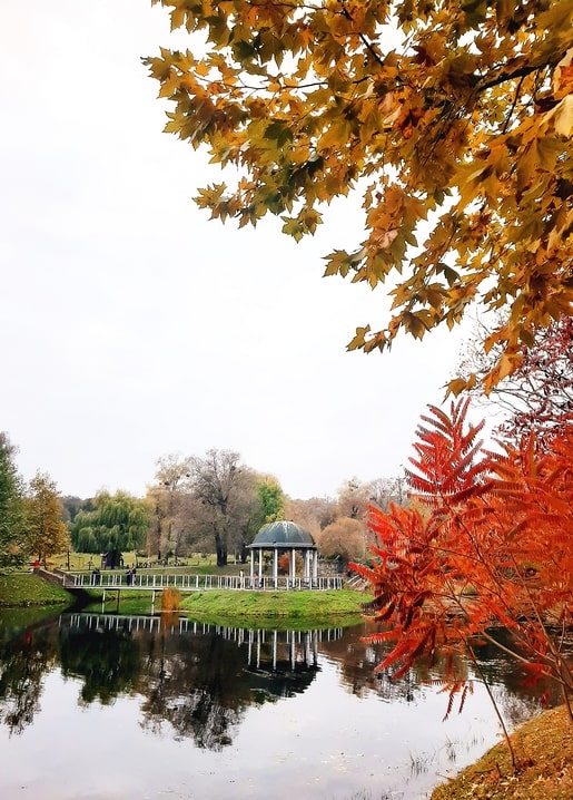 White rotunda beside an autumn pond in Feofania Park, framed by golden maple and red sumac leaves