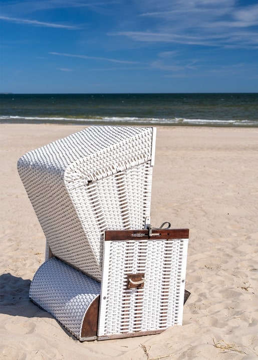 White wicker beach chair standing alone on sand facing a calm blue sea