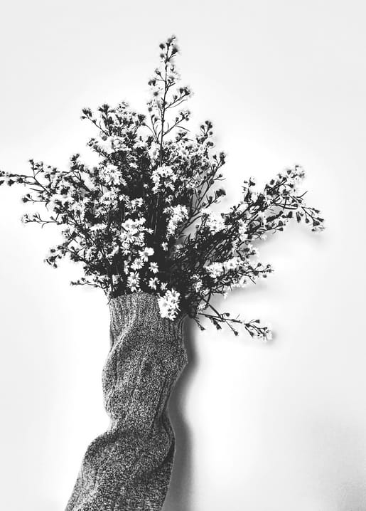 Winzige weiße Wildblumen als Strauß gebunden und in den Ärmel eines Strickpullovers gesteckt