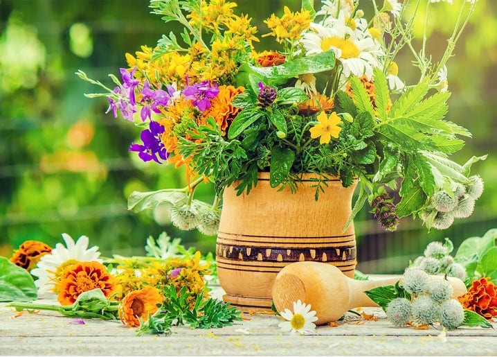 Wooden mortar filled with marigolds, daisies and purple wildflowers on a garden table