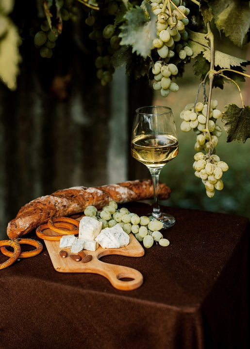 Wine glass, baguette, pretzels, blue cheese and grapes on a wooden board under a hanging grapevine