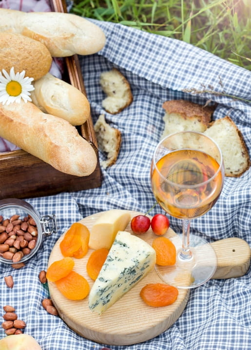 Karierte Picknickdecke mit Wein, Baguette, Blauschimmelkäse, Aprikosen und Gänseblümchen